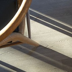Close-up of wooden chair legs casting shadows on a sunlit floor, highlighting the texture of the light wooden surface.