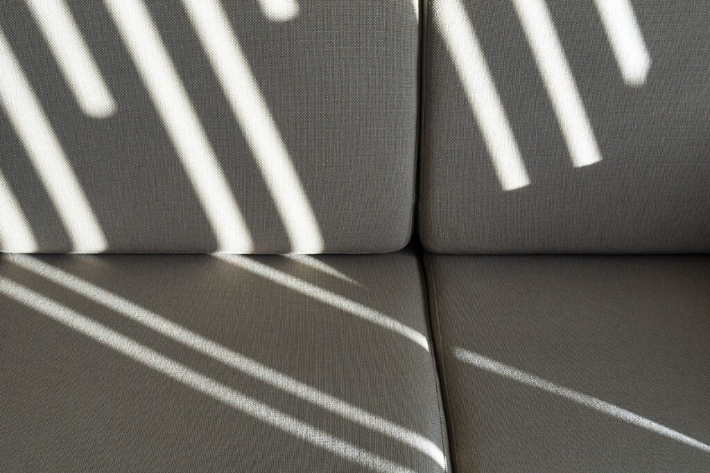 Sunlit shadows create a striped pattern on a textured gray couch, highlighting the sofa's detailed fabric design.