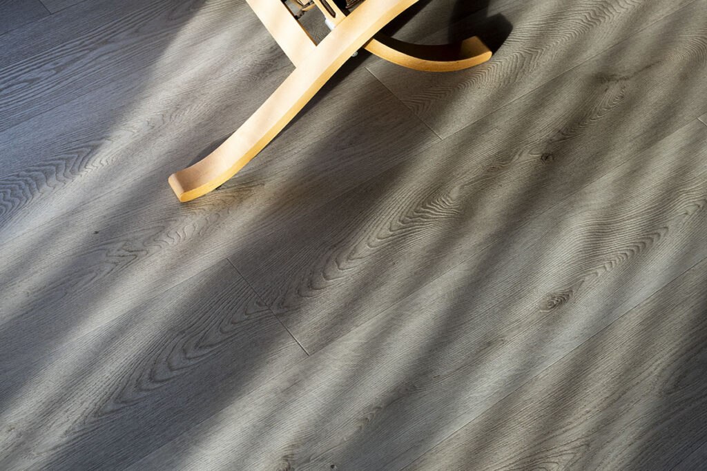 Wooden rocking chair on light gray hardwood flooring, casting intricate shadows across the textured planks.