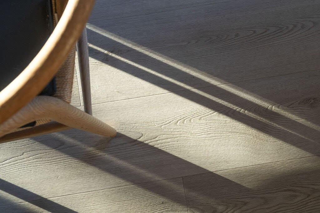 Sunlight casts shadows from a wicker chair onto textured wooden flooring, creating a warm, inviting ambiance.