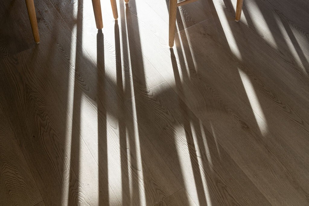 Sunlight casts long shadows of chairs on a hardwood floor, creating an intricate pattern of light and dark.